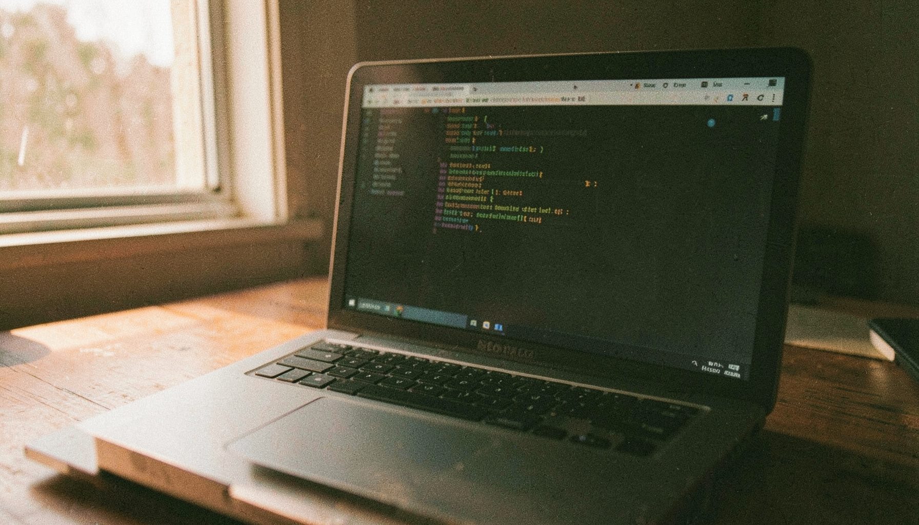 A warm analog film photograph with visible grain showing a laptop screen displaying a Linux terminal window on a wooden desk, with soft natural light from a nearby window.
